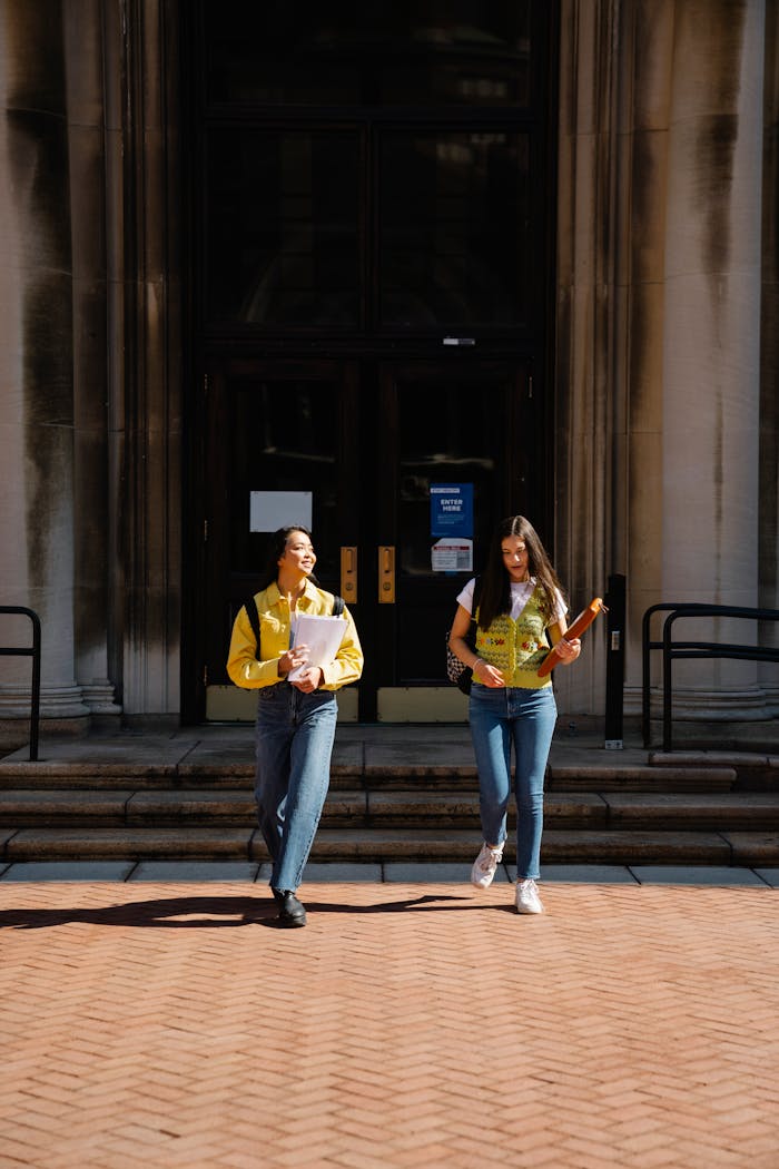 services-04 Two women in casual attire walking together on a university campus during the day.