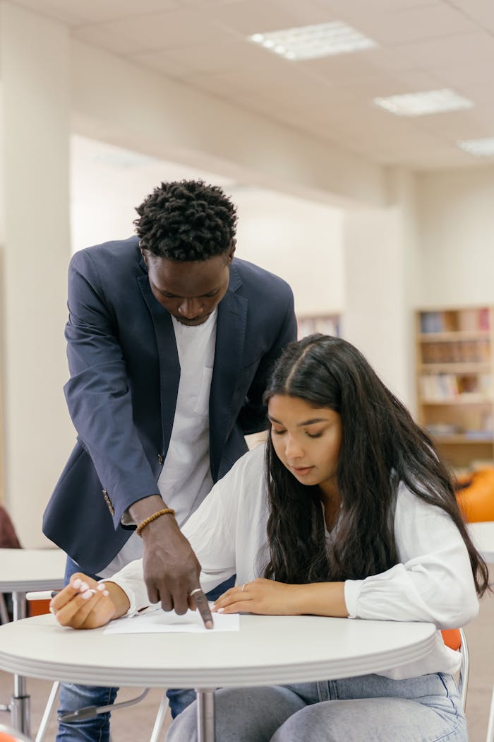 Mastering the First Impression: Your intriguing post title goes here A man tutor guides a woman student during a study session in a library setting.